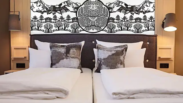 Zwei Betten im Hotelzimmer mit gepolsterter Kopfzeile und schwarzer-weißer Bergwand als Hintergrund.