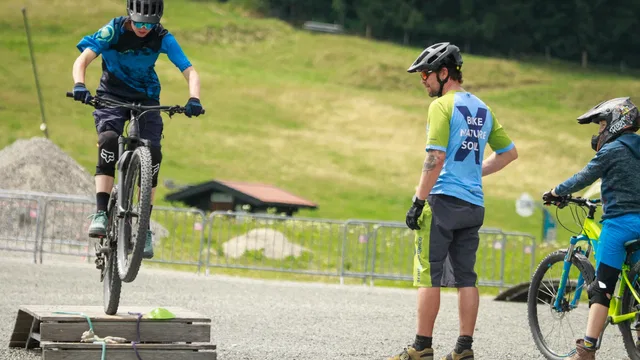 Kind übt mit dem Mountainbike an einem Holzhindernis unter Anleitung eines Trainers