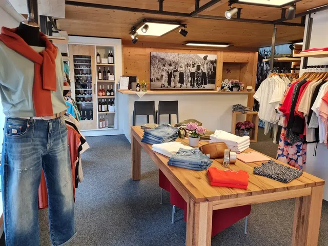 Modedesign-Laden mit Jeansoutfit an der linken Seite, Holztischen und Kleiderstangen.