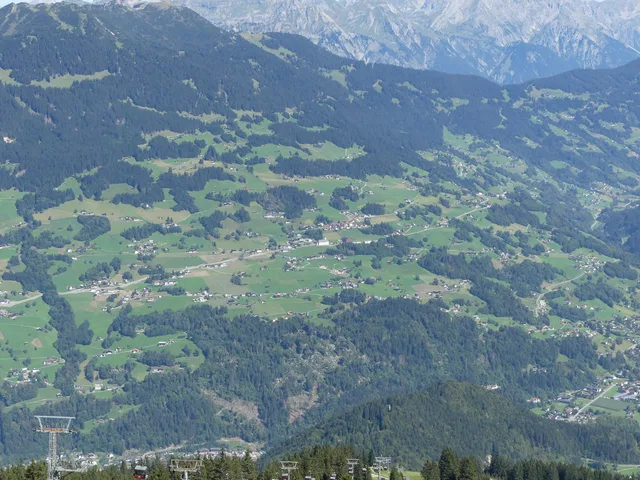 Landschaft mit grünen Tälern, Dörfern und Wald, umgeben von Bergen.
