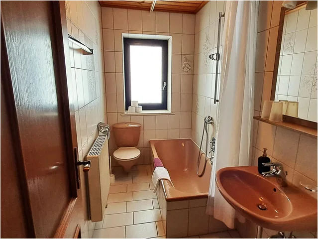 Kleines Badezimmer im Appartement mit pinkfarbener Badewanne, Toilette, Waschbecken, Dusche, Fenster