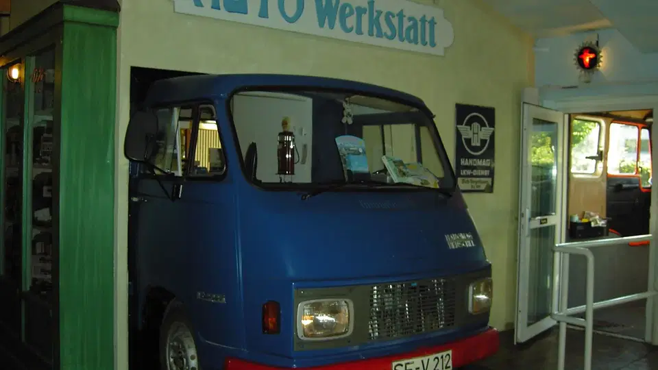 Blauer alter Transporter in einer Auto-Werkstatt vor Schild 'AUTO Werkstatt'