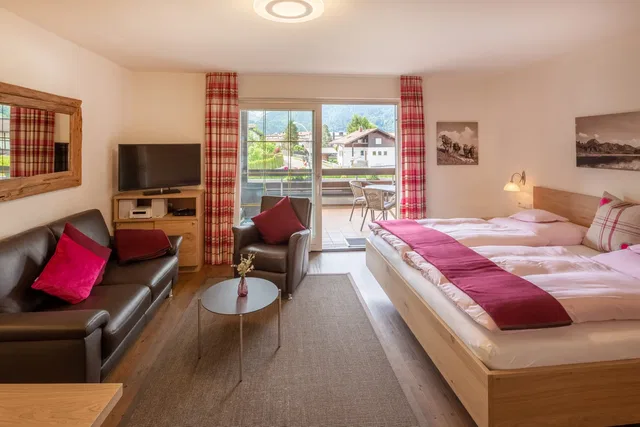 Hotelzimmer mit Doppelbett, Sitzecke, Fernseher und Balkonzugang, rote Akzente.