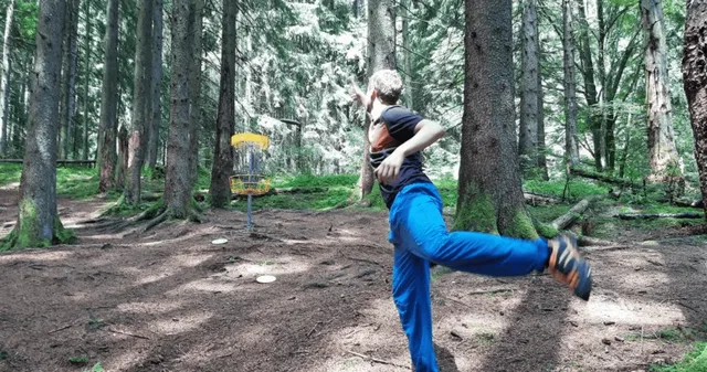 Person wirft Discgolf-Scheibe in Wald