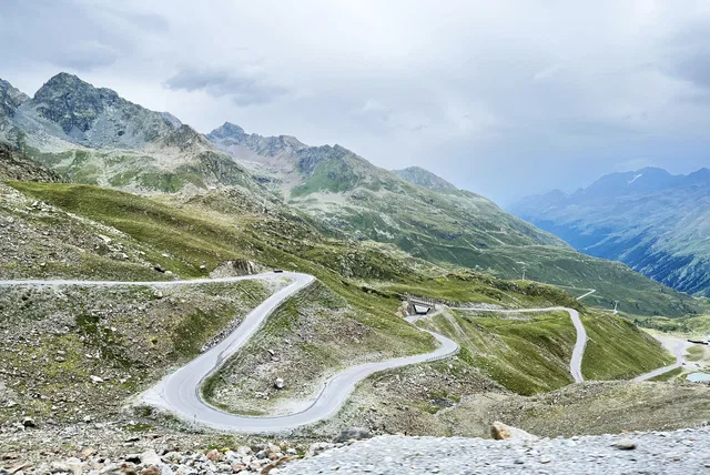 Schmale Serpentinenstraße windet sich durch eine grüne Alpenlandschaft.
