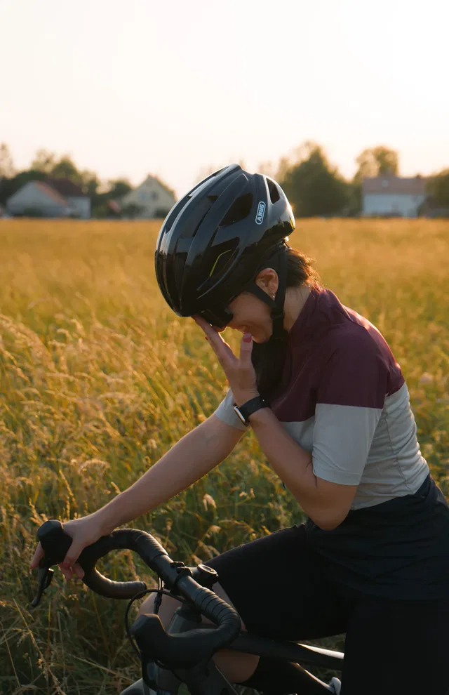 Person mit Fahrradhelm im Feld neben dem Fahrrad bei Sonnenuntergang.