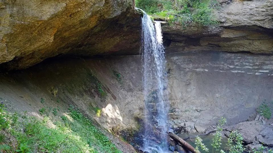 Kleiner Wasserfall fällt von einer Felswand in eine grüne Schlucht.