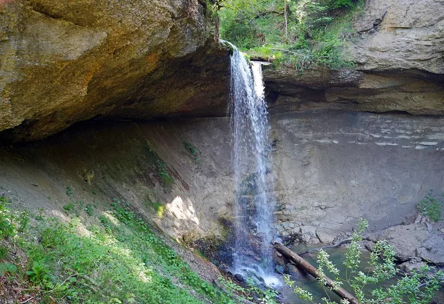 Kleiner Wasserfall fällt von einer Felswand in eine grüne Schlucht.