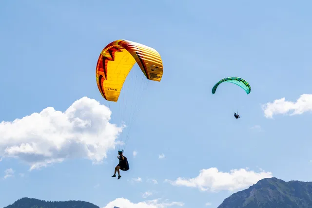 Zwei Gleitschirme fliegen hoch am blauen Himmel über Berge.