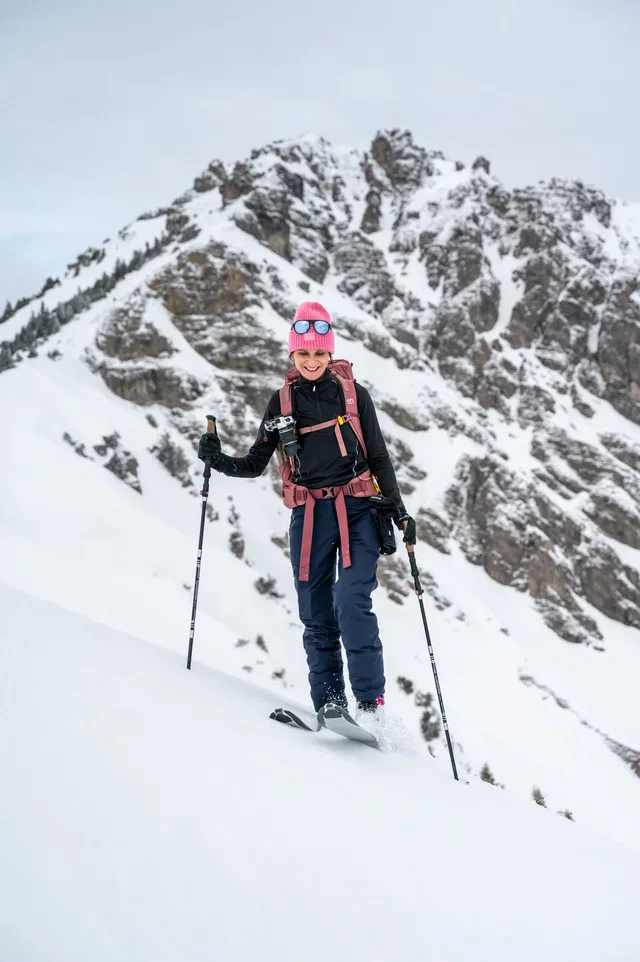 Skitouristin in pinker Mütze mit Skistöcken auf schneetickem Hang