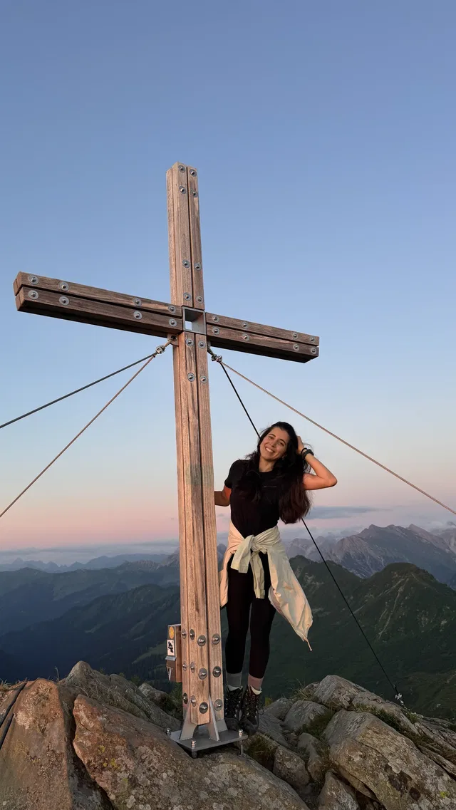 Frau neben Holzkreuz auf Berggipfel bei Sonnenuntergang