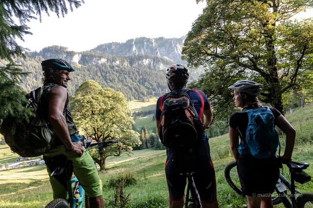 Drei Mountainbiker bei einer Pause mit Blick auf bewaldete Berge