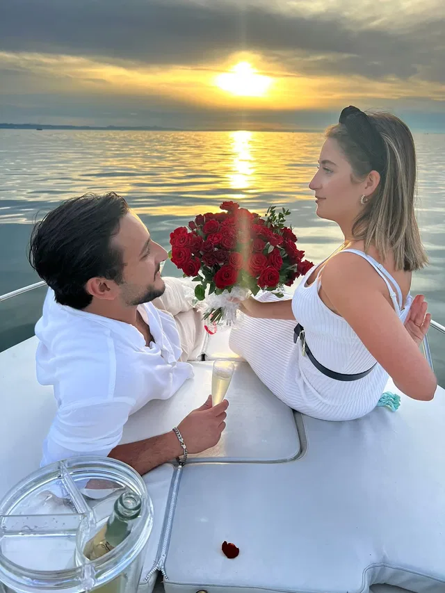 Paar auf einem Boot mit Rosenstrauß bei Sonnenuntergang auf dem Meer.