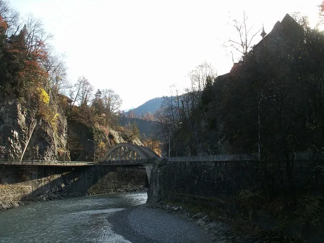 Steinbogenbrücke über Fluss mit felsigen Ufern und Herbstbäumen