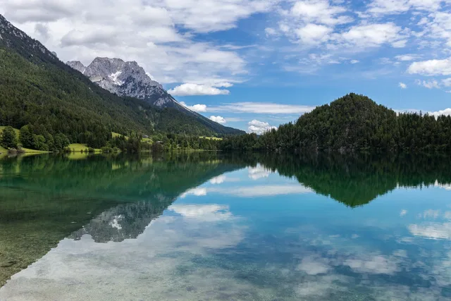 Bergsee mit Spiegelung von bewaldeten Hängen und schroffen Gipfeln