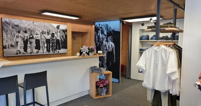 Modegeschäft: Weiße Bluse am Kleiderständer, Holzkounter, Schwarz-Weiß-Bilder an der Wand.