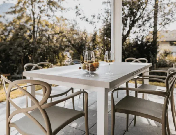 Weißer Outdoor-Gartentisch mit vier Stühlen, zwei Weingläsern und Obstschale