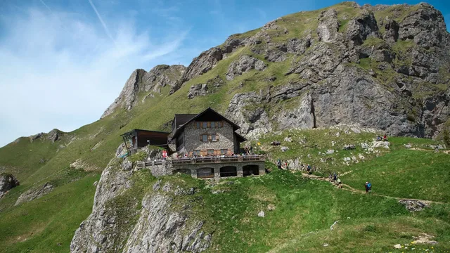 Steinerne Berghütte an einer felsigen Bergwand mit grünen Wiesen