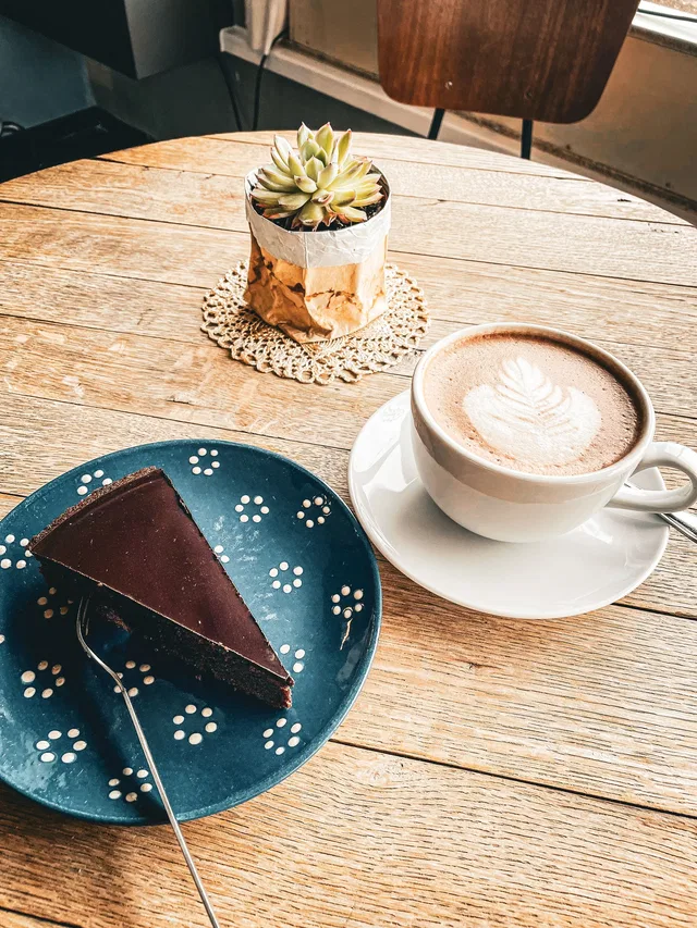 Kleiner Schokoladenkuchen auf blauem Teller neben Cappuccino