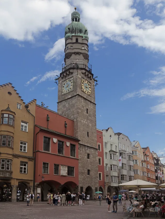Historischer Uhrturm mit grüner Kuppel an einem belebten Stadtplatz