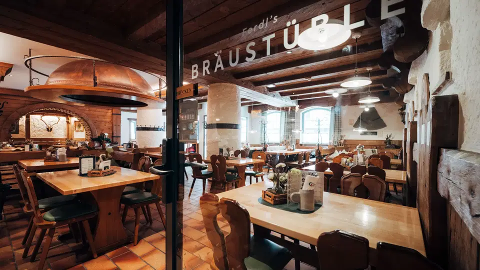 Rustikales Brauhaus-Interieur mit Holzbalken, Holztischen und gemütlicher Beleuchtung.