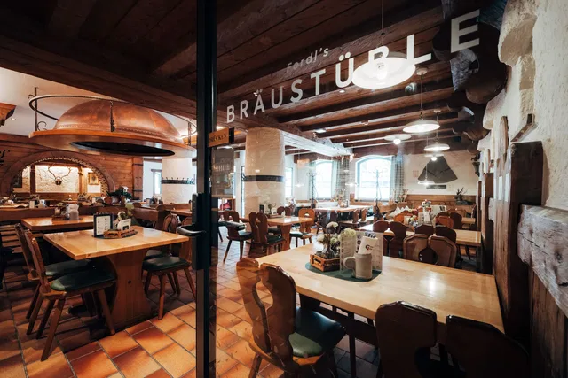 Rustikales Brauhaus-Interieur mit Holzbalken, Holztischen und gemütlicher Beleuchtung.