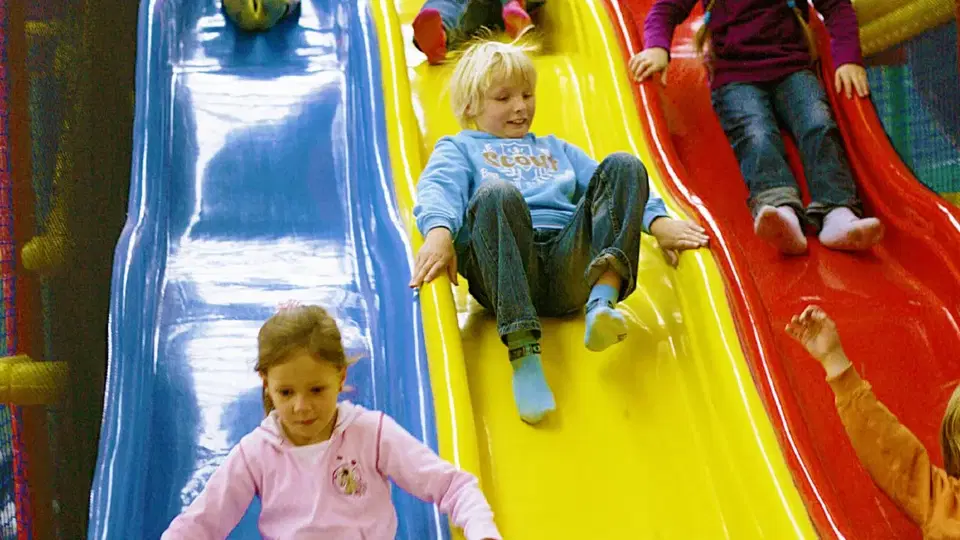 Kinder rutschen in einer bunten Indoor-Spielanlage die Rutschen hinunter.