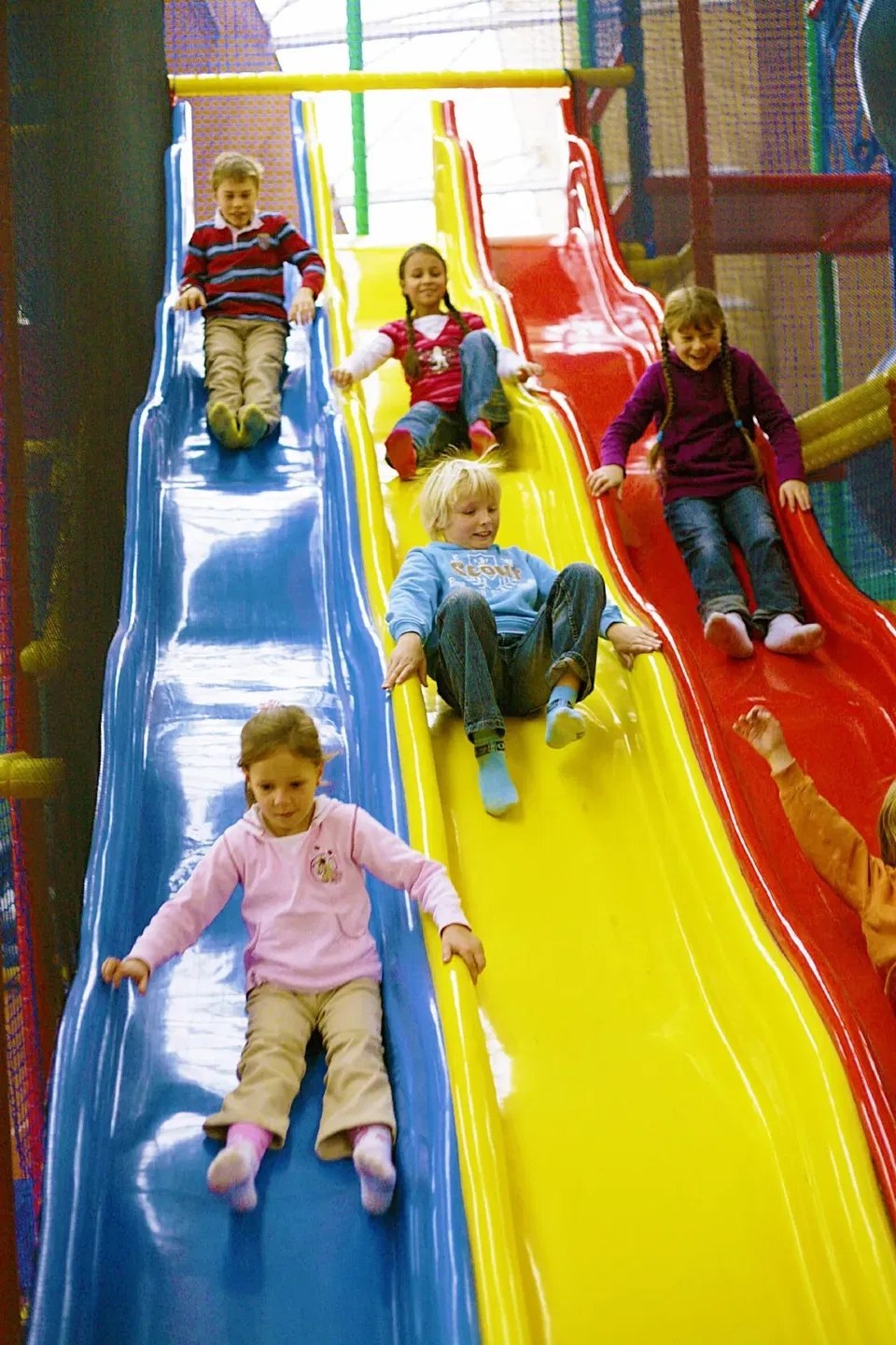 Kinder rutschen in einer bunten Indoor-Spielanlage die Rutschen hinunter.