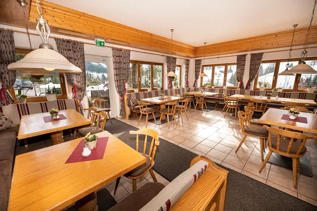 Gemütliches Restaurant mit Holztischen, Stühlen und großen Fensterfronten.
