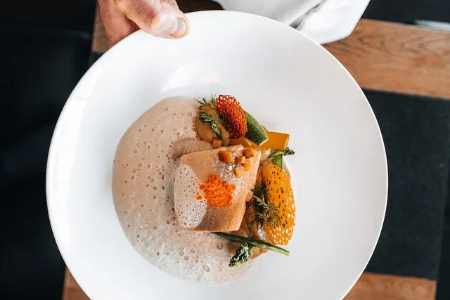Nahaufnahme eines weißen Tellers mit Fisch, Gemüse und Schaum