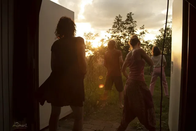 Gruppe von Menschen steht im Türrahmen eines Hauses beim Sonnenuntergang, Rückenansicht, draußen in der Natur.