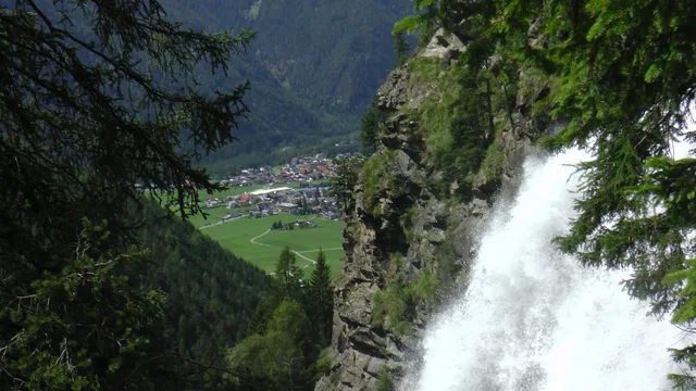 Wasserfall stürzt an felsiger Klippe herab, Dorf im Tal sichtbar