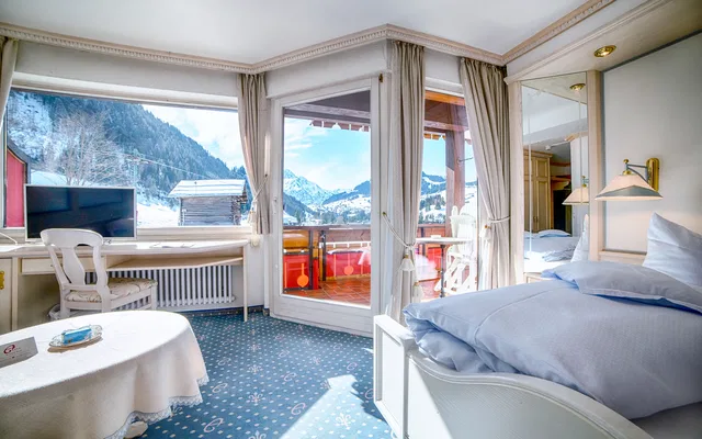 Hotelzimmer mit Balkonzugang, Blick auf verschneite Berge, Bett und Arbeitsbereich.
