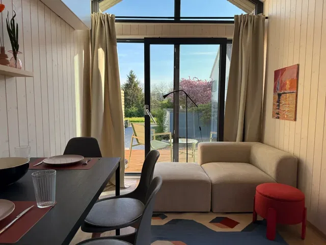 Wohnbereich eines Ferienhauses mit Sofa, Esstisch und Blick nach draußen durch große Glasfront
