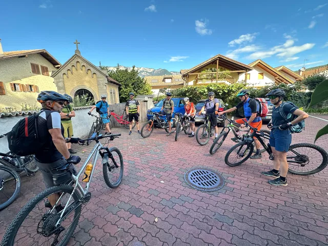 Mountainbike-Gruppe vor einer Kapelle mit Bergen im Hintergrund