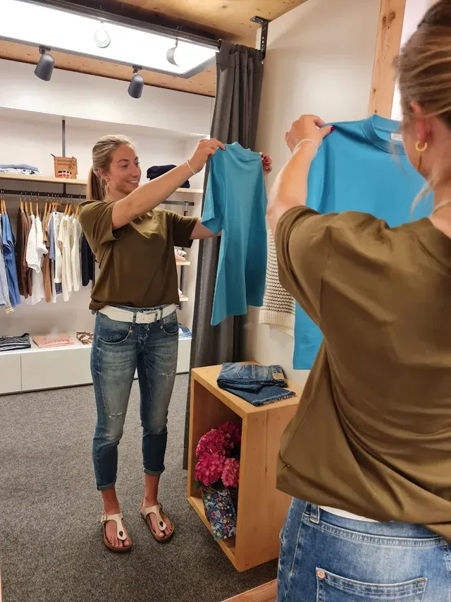 Zwei Frauen in einem Kleidershop halten blaue T-Shirts hoch.