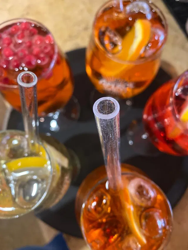 Mehrere Cocktails in Gläsern mit Strohhalmen, Eis und Orangenscheiben