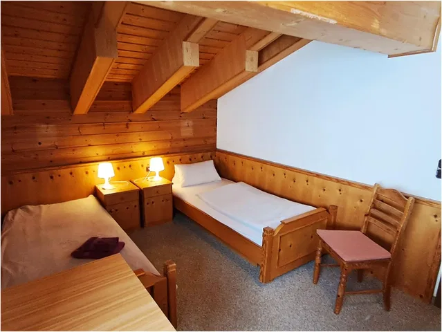 Dachgeschoss-Schlafzimmer aus Holz mit zwei Einzelbetten, Nachttischenlampen und Holzmöbeln.