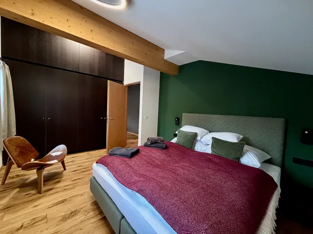 Schlafzimmer mit grüner Akzentwand, großem Bett, rotem Überwurf, Holzboden und dunklen Schränken.