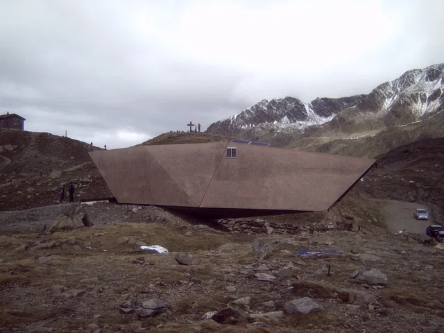 Kantiges, braunes Gebäude in einer kargen Berglandschaft mit verschneiten Bergen dahinter.