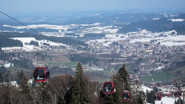 Rote Gondeln der Seilbahn ziehen durch verschneite Berglandschaft über ein Dorf.
