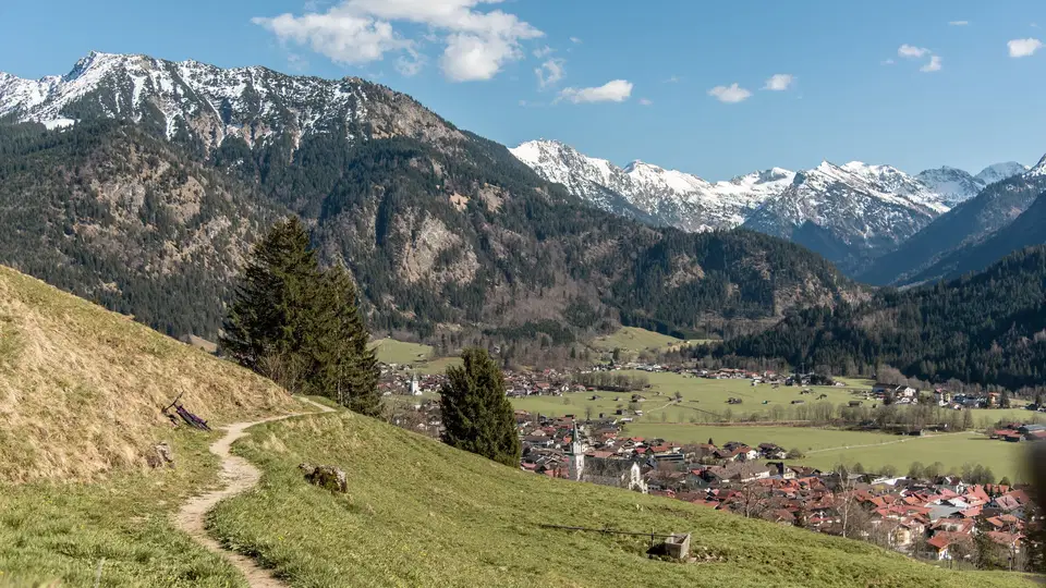Wanderweg am Hang mit Blick auf Tal und verschneite Berge