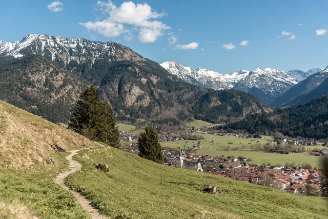 Wanderweg am Hang mit Blick auf Tal und verschneite Berge
