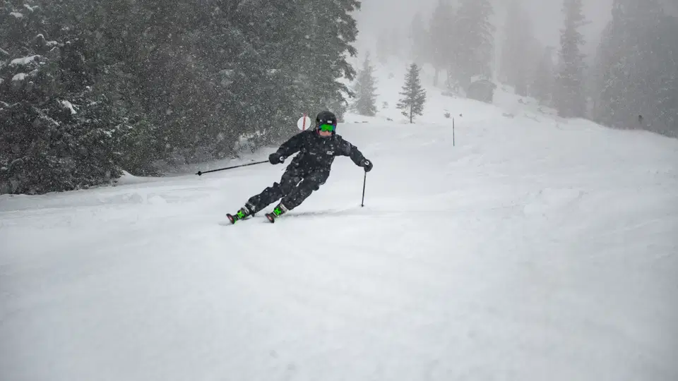 Skifahrer in dunkler Skiausrüstung auf verschneiter Piste mit fallendem Schnee