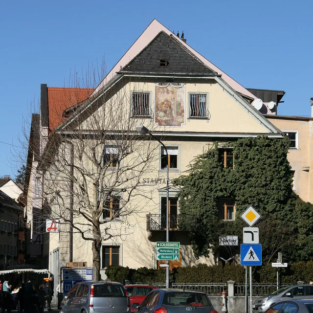 Mehrstöckiges Gebäude mit Giebeldach, Straßenszene mit Fahrzeugen und Verkehrsschildern
