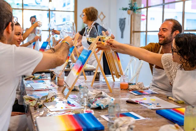 Teilnehmende stoßen zwischen bemalten Leinwänden im KreativEvents-Studio an.