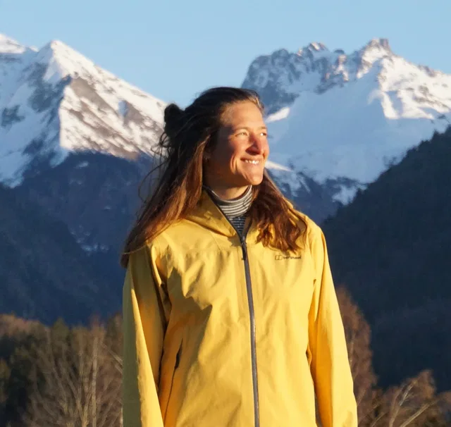 Frau in gelber Outdoorjacke vor schneebedeckten Bergen