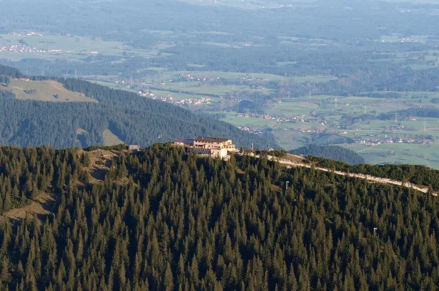 Gebäude auf einem Waldgipfel mit Straßenzug, umgeben von Tannenwald und weiter Tallandschaft.