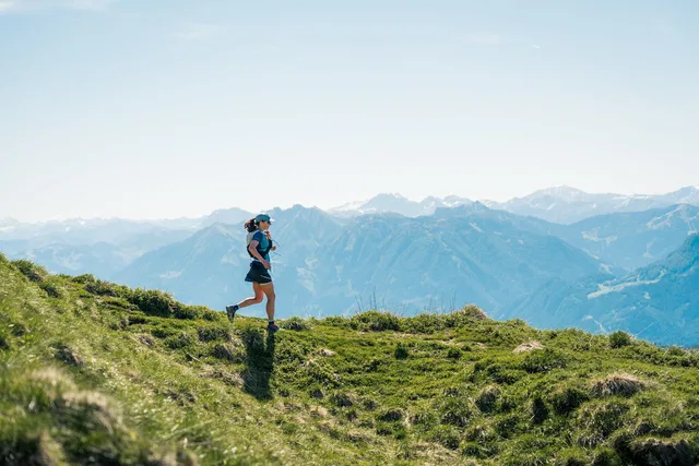 Läuferin auf einem Berggrat vor einer weiten Bergkulisse
