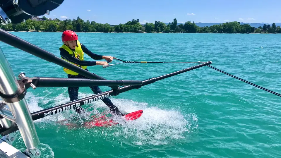 Wakeboarder wird von einem Boot mit Seil über das Wasser gezogen, roter Helm, gelbe Rettungsweste.
